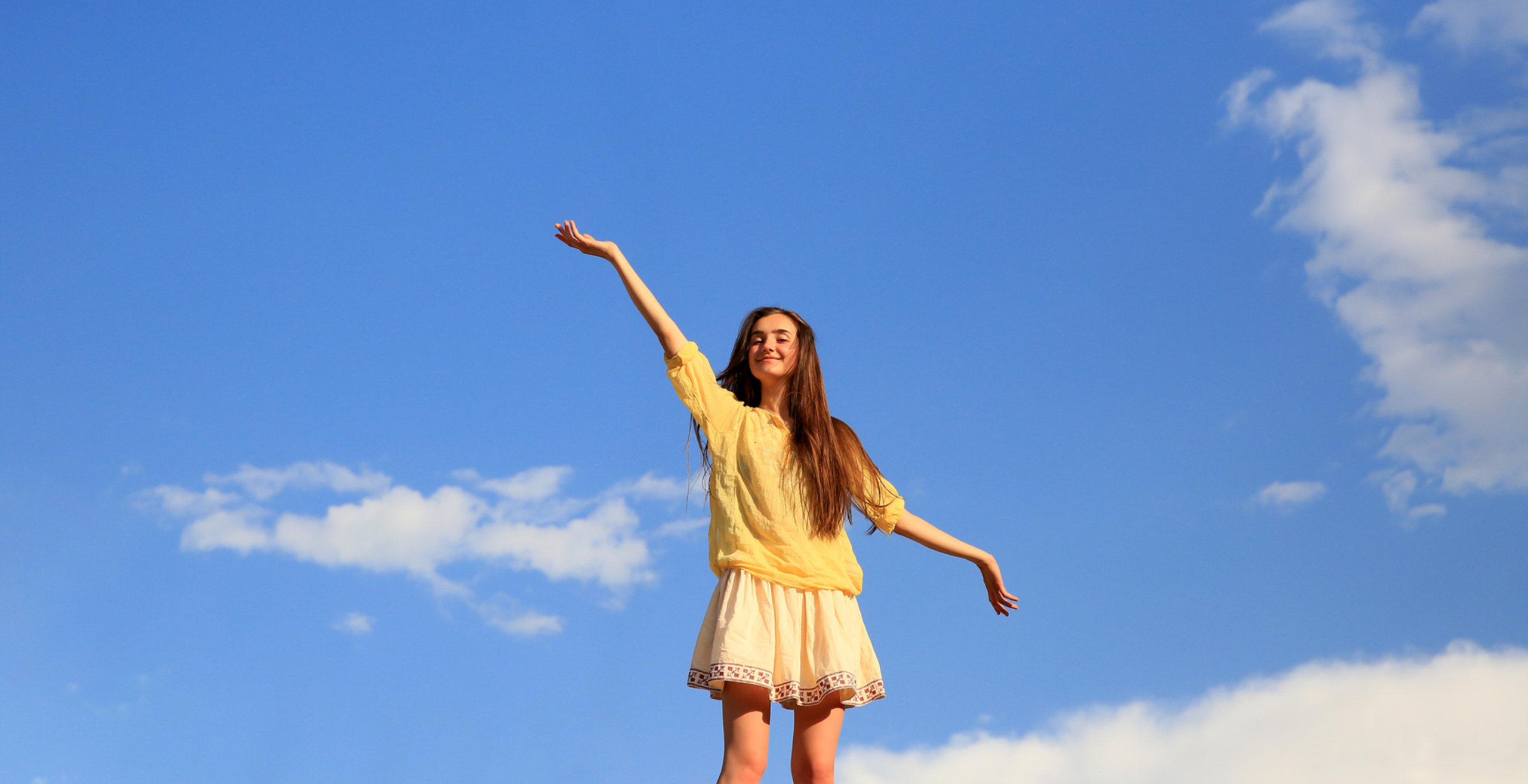 Diya Mathew raising her arms in joy against a blue sky